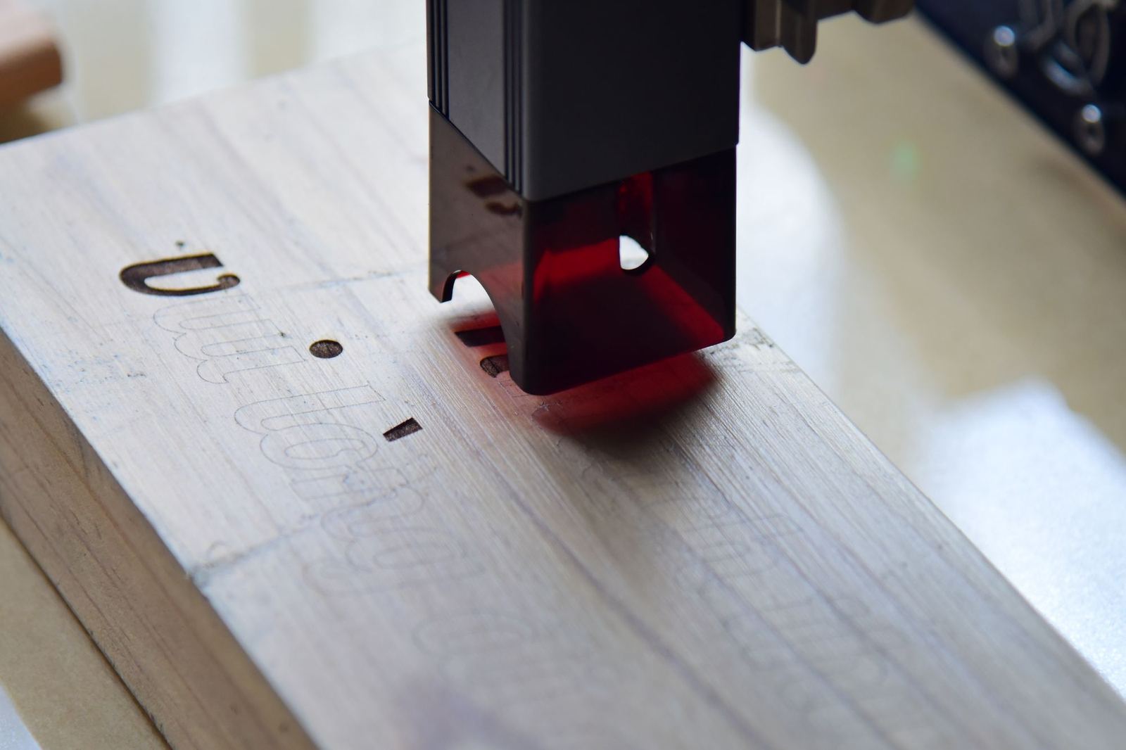 Laser cutting head tracing a design into plywood